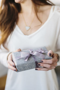 A woman holding a package with a large ribbon wrapped around it. 