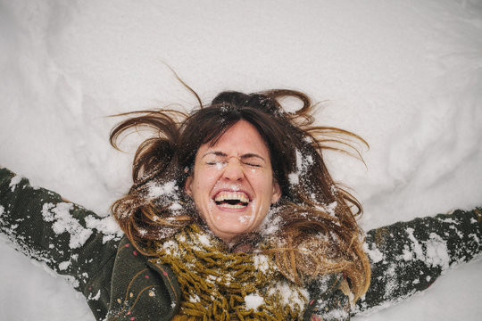 A woman lying on a snow bank with her arms stretched out. 