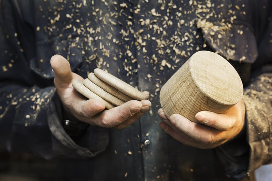Close up of a man in a carpentry workshop, holding a wooden shape and wooden discs in his hands.
