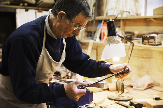 Man standing at a work bench in a carpentry workshop, working on a piece of wood secured in a bench vice.
