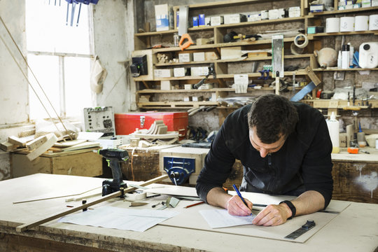 Man standing at a work bench in a carpentry workshop, writing a spreadsheet.