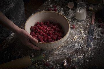Woman holding bowl of fresh raspberries on  floury table