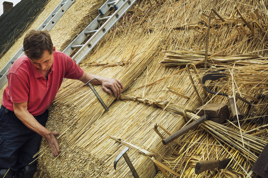 Man thatching a roof, thatching tools, including a wooden mallet, and shearing hooks.