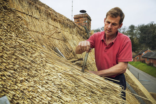Man thatching a roof, inserting a metal peg into the straw.