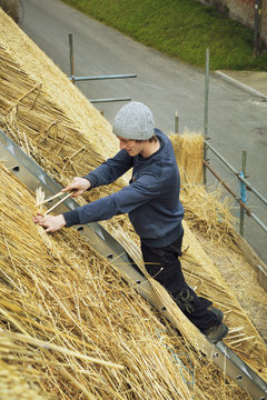 High angle view of a thatcher standing on a ladder on a thatched roof.