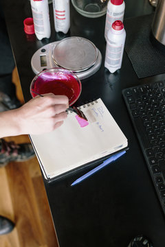 A colourist mixing hair dye using powder and water, and testing the colour on paper.