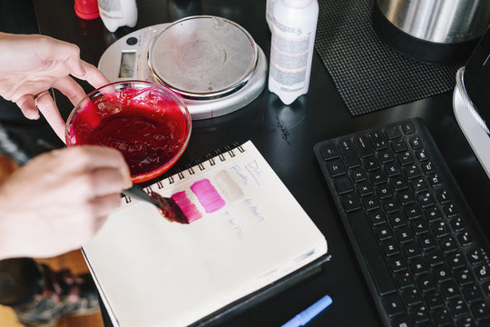 A colourist mixing hair dye using powder and water, and testing the colour on paper.