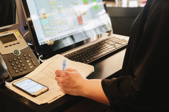 A person working at a hair salon reception, laptop computer, landline phone, diary and smart phone on the desk. 