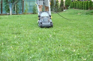 Man is pushing a mower to cut the grass in his garden