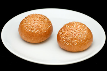 Two sandwich buns with sesame on white plate