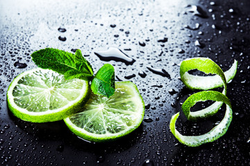 Plakat Green limes with mint and water drops on black background