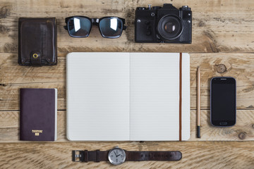 Travel journal surrounded by travelling related items including passport wallet sunglasses camera smartphone and watch