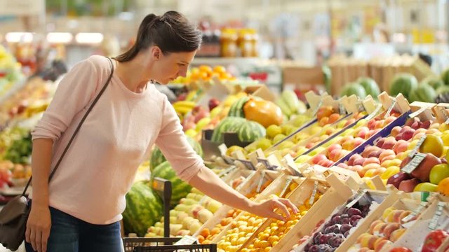 The girl in a supermarket selects the fruit.