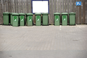 Gr&uuml;ne M&uuml;llcontainer vor Bretterzaun / Eine Reihe gr&uuml;ner M&uuml;llcontainer f&uuml;r Glasabfall steht vor einem Bretterzaun.