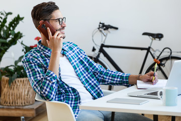Handsome young man working with laptop and mobile phone at home.