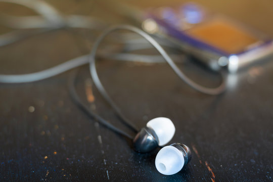 Pocket music player with in-ear headphones on black wooden background