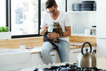 Handsome young man playing with cat in the kitchen.