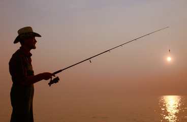 fisherman with a fishing rod on the background of sunset. dark silhouette of a fisherman with a fishing rod in the hands who is trying to catch the setting sun. the concept of aging
