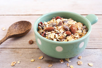 A healthy bowl of muesli with oats, nuts and dried fruit on a wooden table.