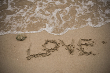 love handwritten on a sandy beach with wave on background