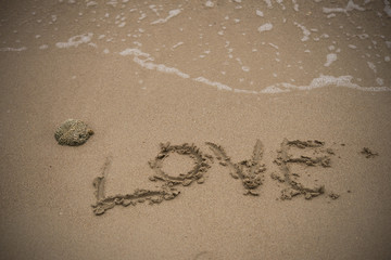 love handwritten on a sandy beach with wave on background