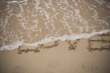Fototapeta na wymiar love handwritten on a sandy beach with wave on background