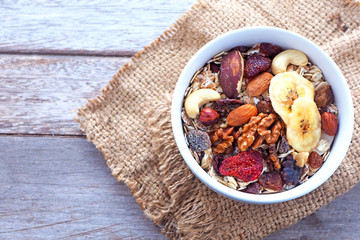 Top view of a healthy bowl of muesli with dried fruit and nuts on a wooden table.