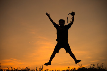 silhouette of man overjoy jump by holding camera at sunrise