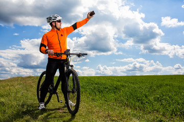 Obraz na płótnie Canvas Young Cyclist In Orange Shirt Checks His Phone