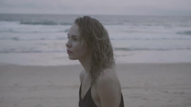 Beautiful blonde glamour woman wearing black dress walking on a beach in a late summer afternoon with wet hair over sea and sky background -video in slow motion