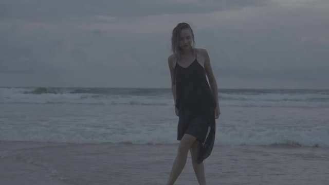 Beautiful blonde glamour woman wearing black dress posing on a beach in a late summer afternoon with wet hair over sea and sky background