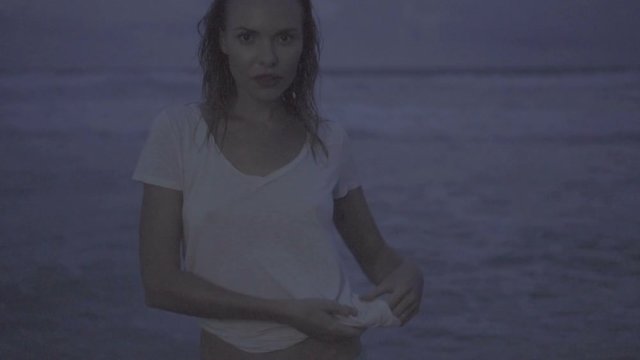 Beautiful blonde sexy woman wearing t-shirt posing on a beach during summer evening with wet hair - video in slow motion