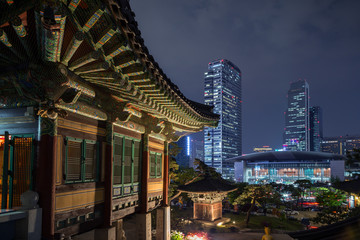 Naklejka premium Ornate building at the Bongeunsa Temple and view of Gangnam in Seoul, South Korea at night.