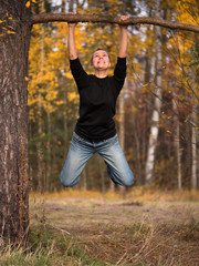 Young woman hanging on a branch with a strained expression on his face on blurred background foliage