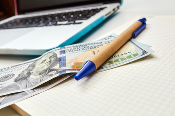 Close-up of money with pen on a notepad. Notepad checkered. Freelance desktop with accessories.