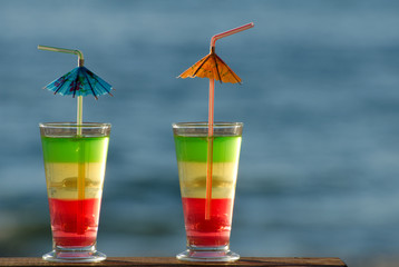 Two glasses with colored cocktails closeup on sea background