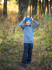 Naklejka na ściany i meble Little boy in hat standing in the grass and shows horns on a blurred background