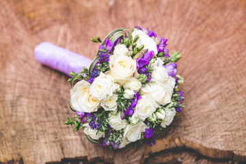 Wedding bouquet with white and violet flowers on nature wooden background.