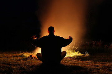 Silhouette of a man sitting in the lotus position at night by th
