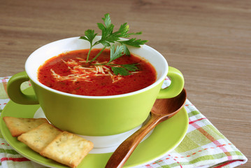 Tomato soup in a green cup on a wooden table.