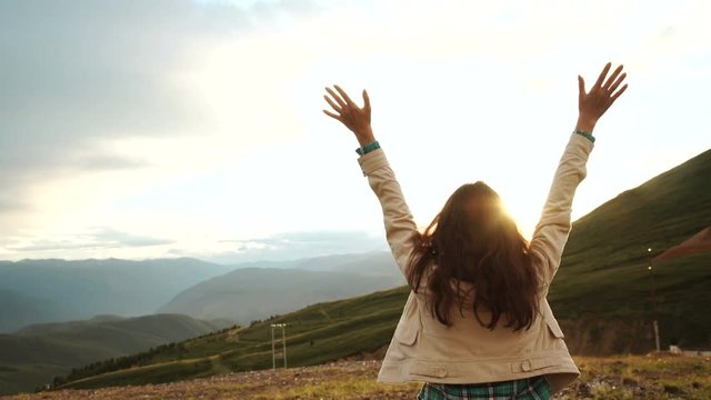 Happy celebrating winning success woman at sunset or sunrise standing elated with arms raised up above her head in celebration of having reached mountain top summit goal during hiking travel trek