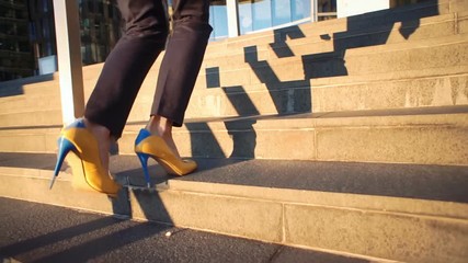 Slow motion. Young beautiful girl in a yellow shoes on hi heels coming up the stairs. Cinematic style video. View on legs and yellow-blue shoes.