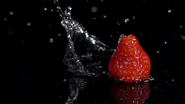 fruit splashing,strawberries falling on wet black surface slow motion