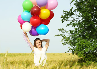 Happy woman with colorful balloons in field on blue sky background