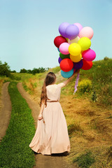 Happy woman with colorful balloons on countryside road