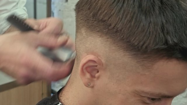 Hairdresser cutting with trimmer hair of man client at beauty parlour