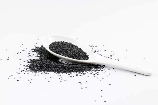 Pile of black sesame seeds with white spoon is isolated white background