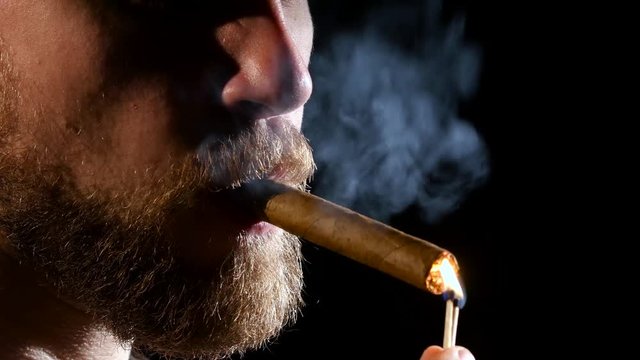 Man in a dark room, smoking a cigar. Close up