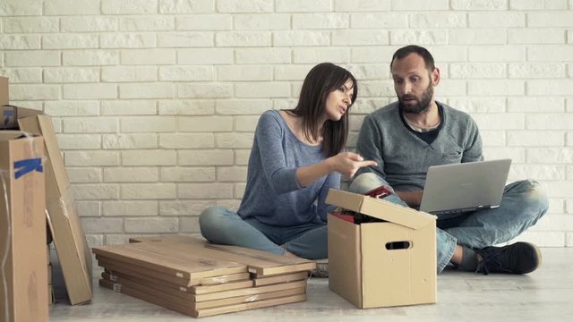 Young couple with laptop and smartphone fighting at their new home
