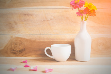 Coffee cup and flower in white pot on wooden floor on morning sunlight. vintage color tone